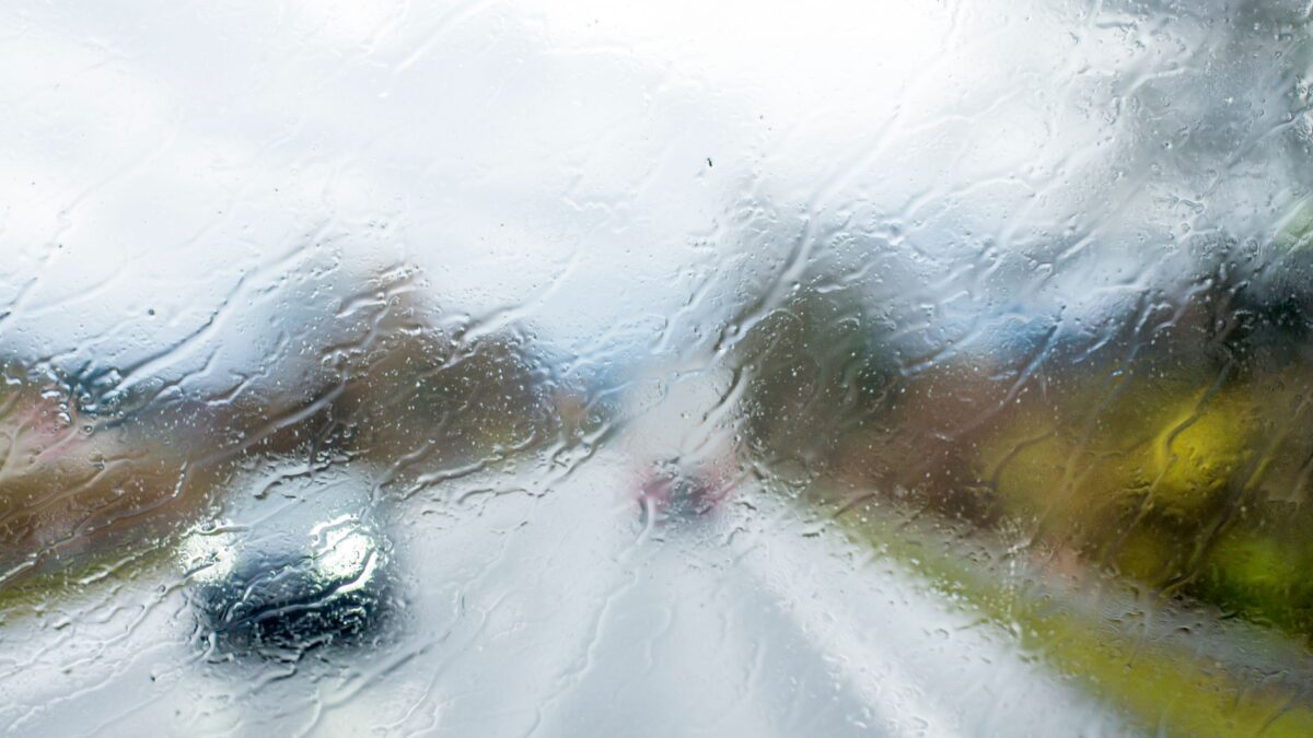 Vue depuis l'intérieur d'un véhicule à travers un pare-brise couvert de gouttes de pluie, avec une route mouillée et des véhicules flous aux phares allumés.