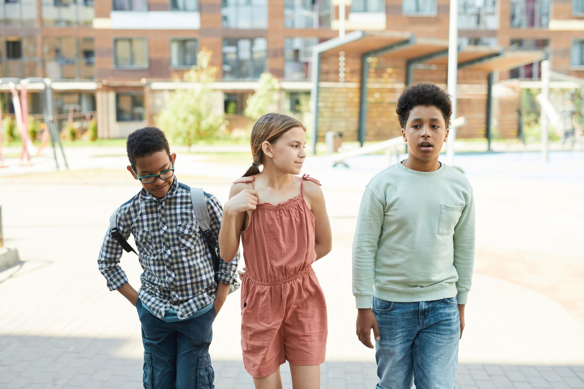 Trois enfants marchant à l'extérieur près d'une école de la ville, montrant la diversité et la solidarité.