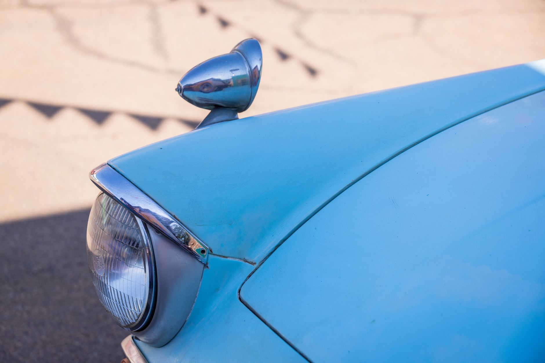 Détail de l’aile avant et du phare d’une voiture ancienne de couleur bleu clair.