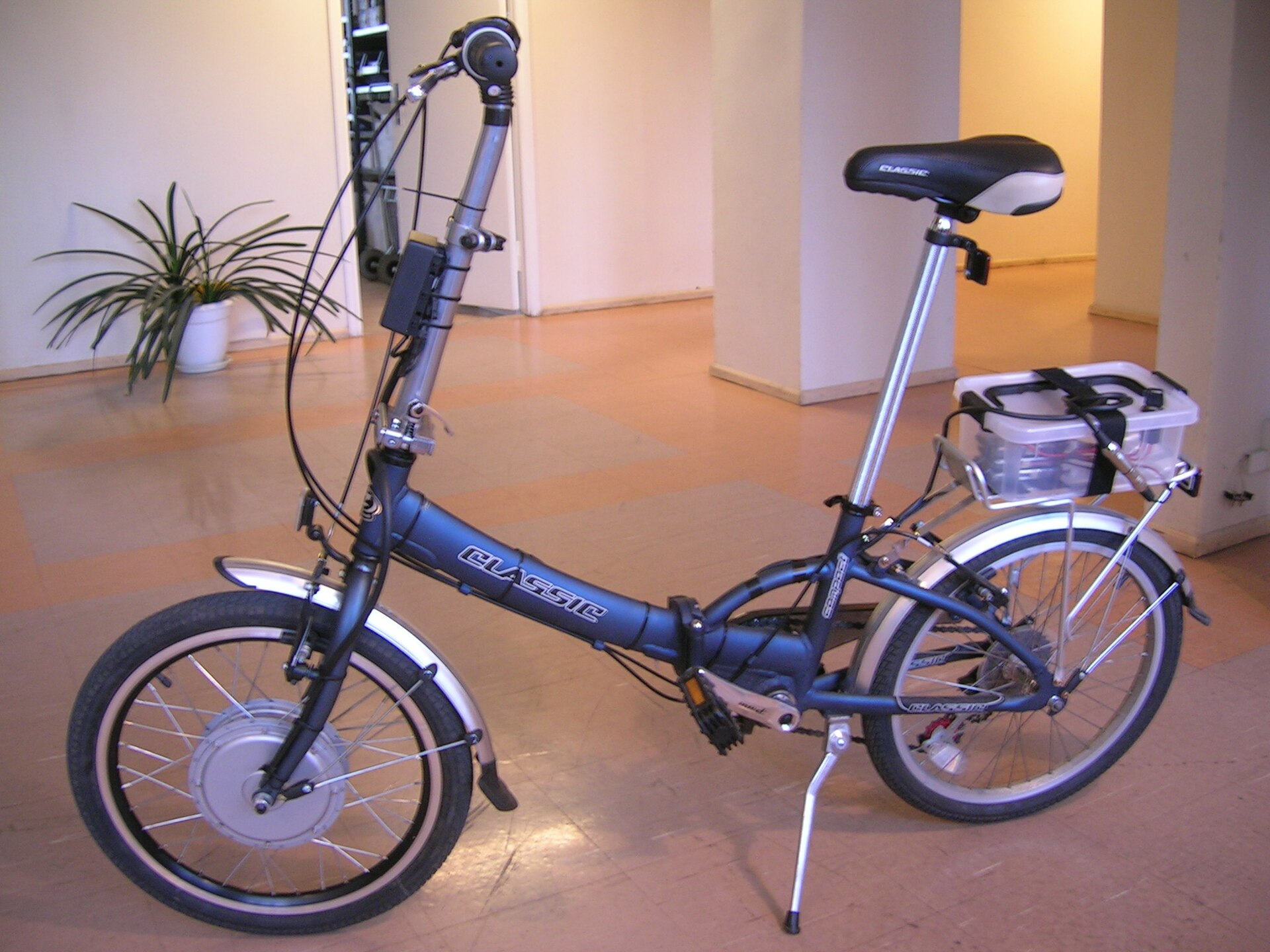 Un vélo électrique pliant bleu à moteur dans la roue avant, garé sur sa béquille