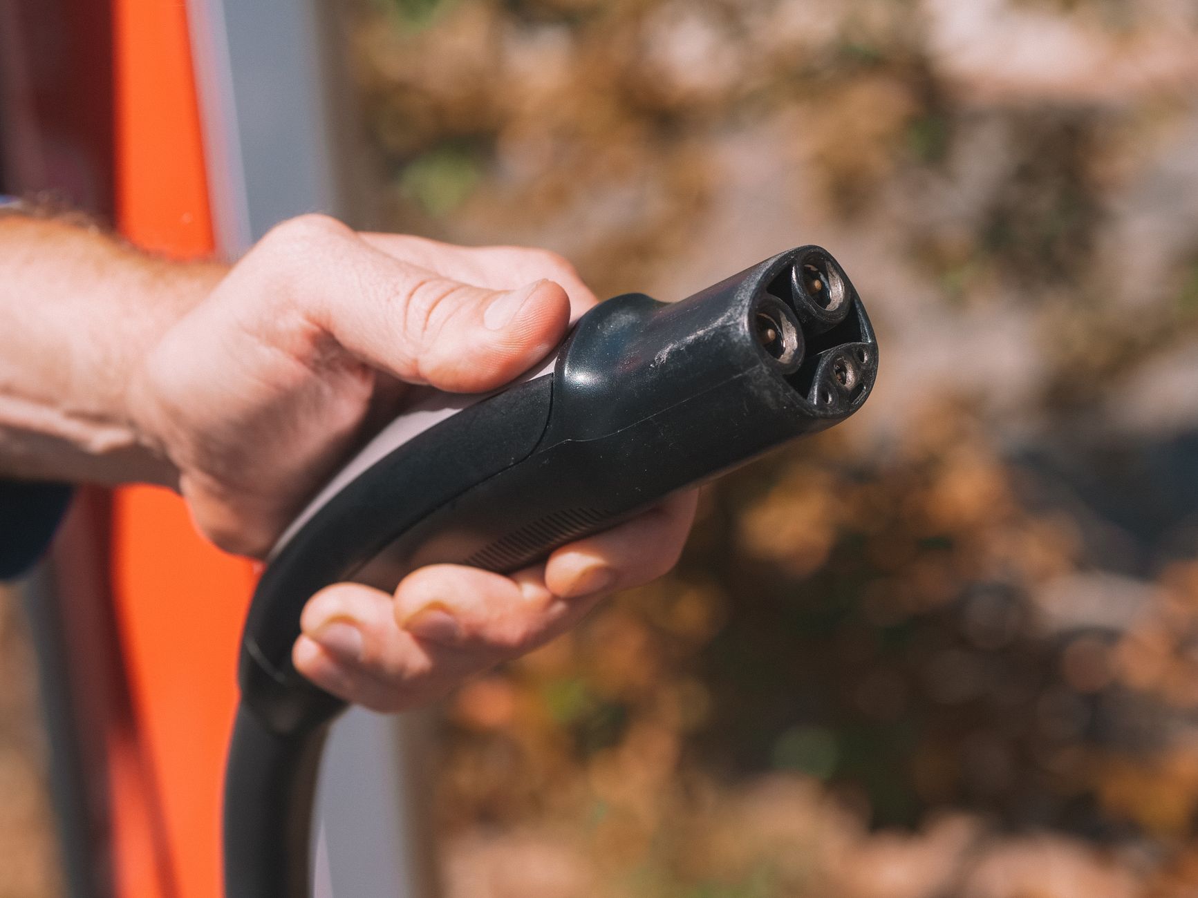 Une main manipule un connecteur de recharge automobile.